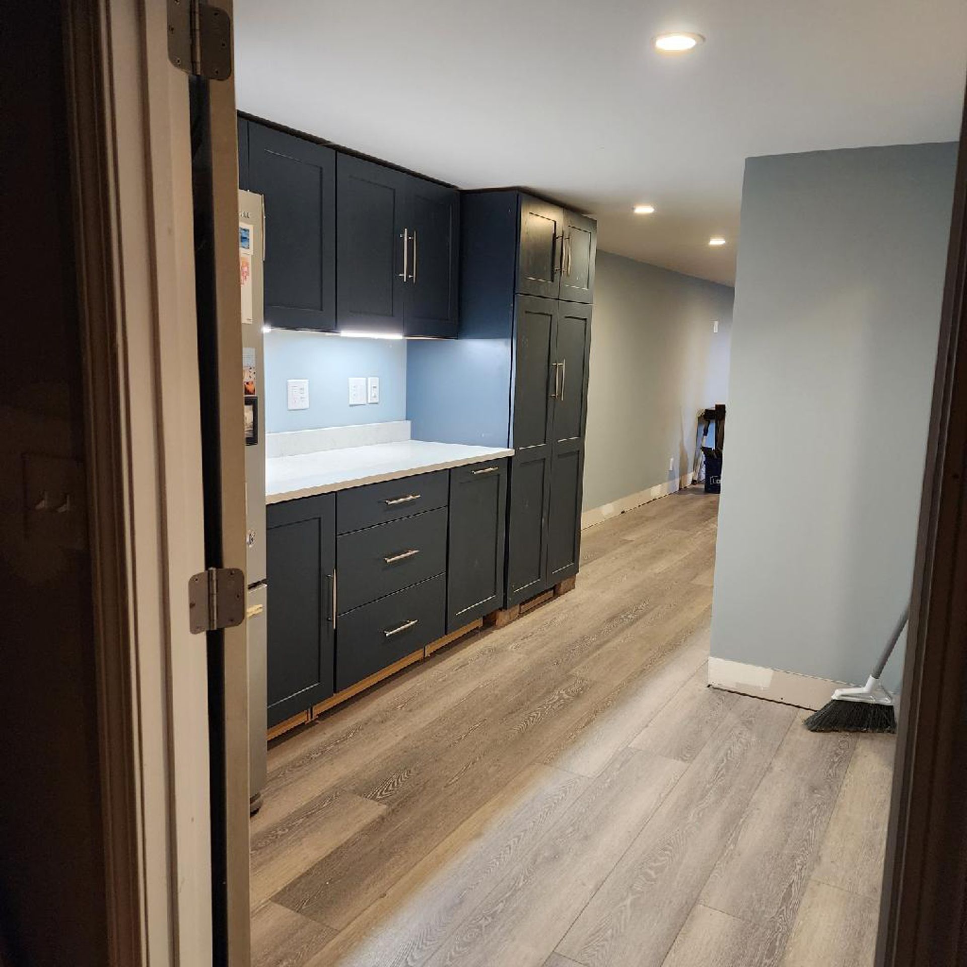 A kitchen with a refrigerator and a broom on the floor