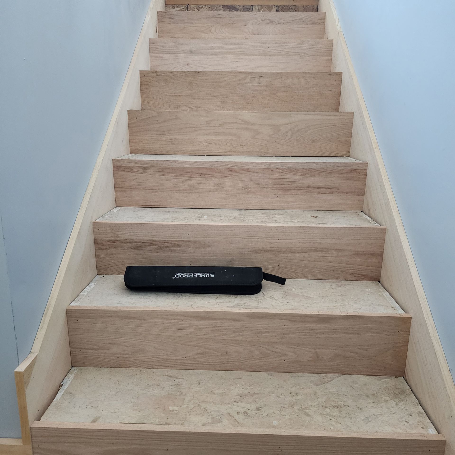 A wooden staircase with a black case on the bottom step