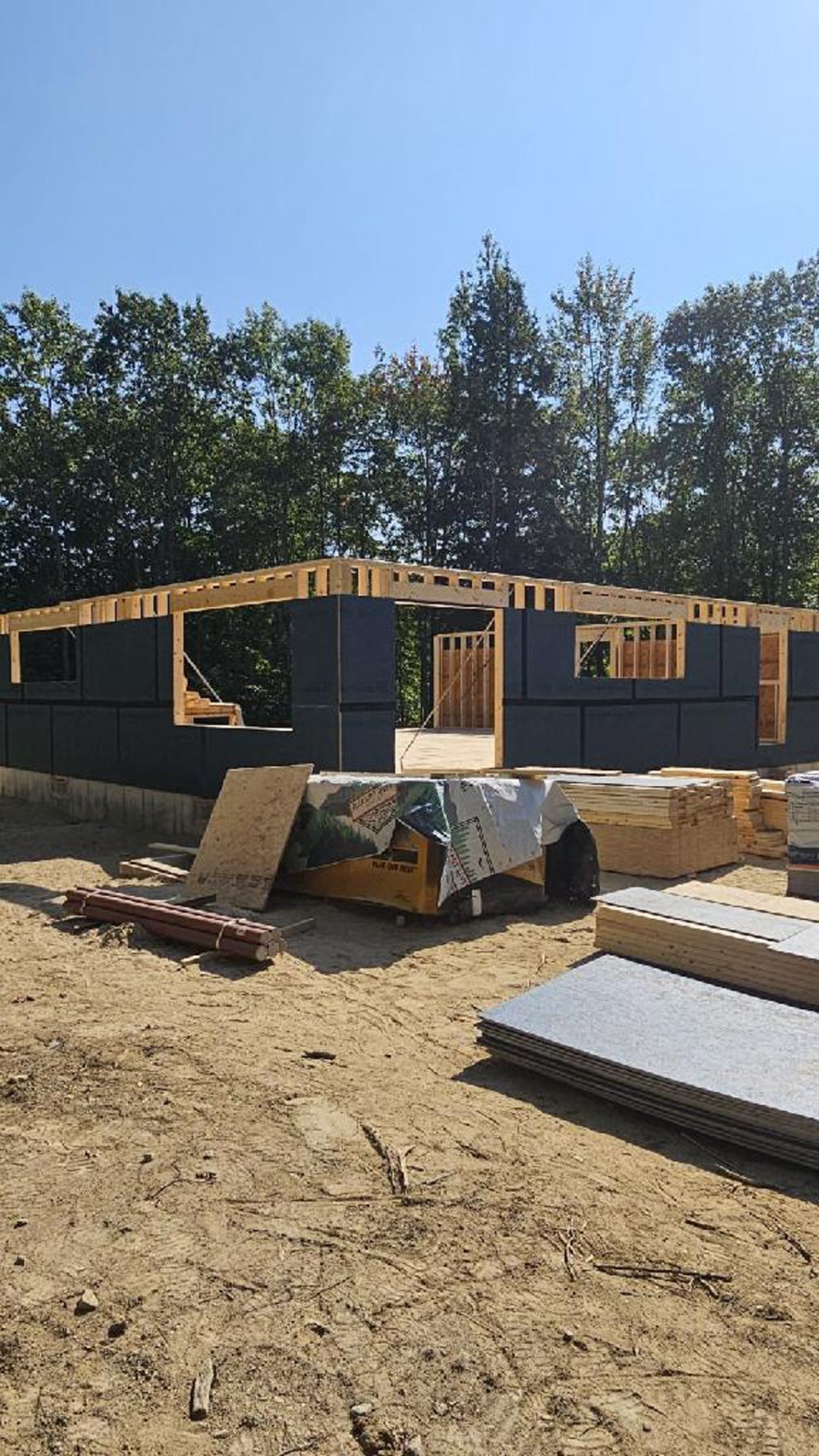 A house is being built in a dirt field with trees in the background.