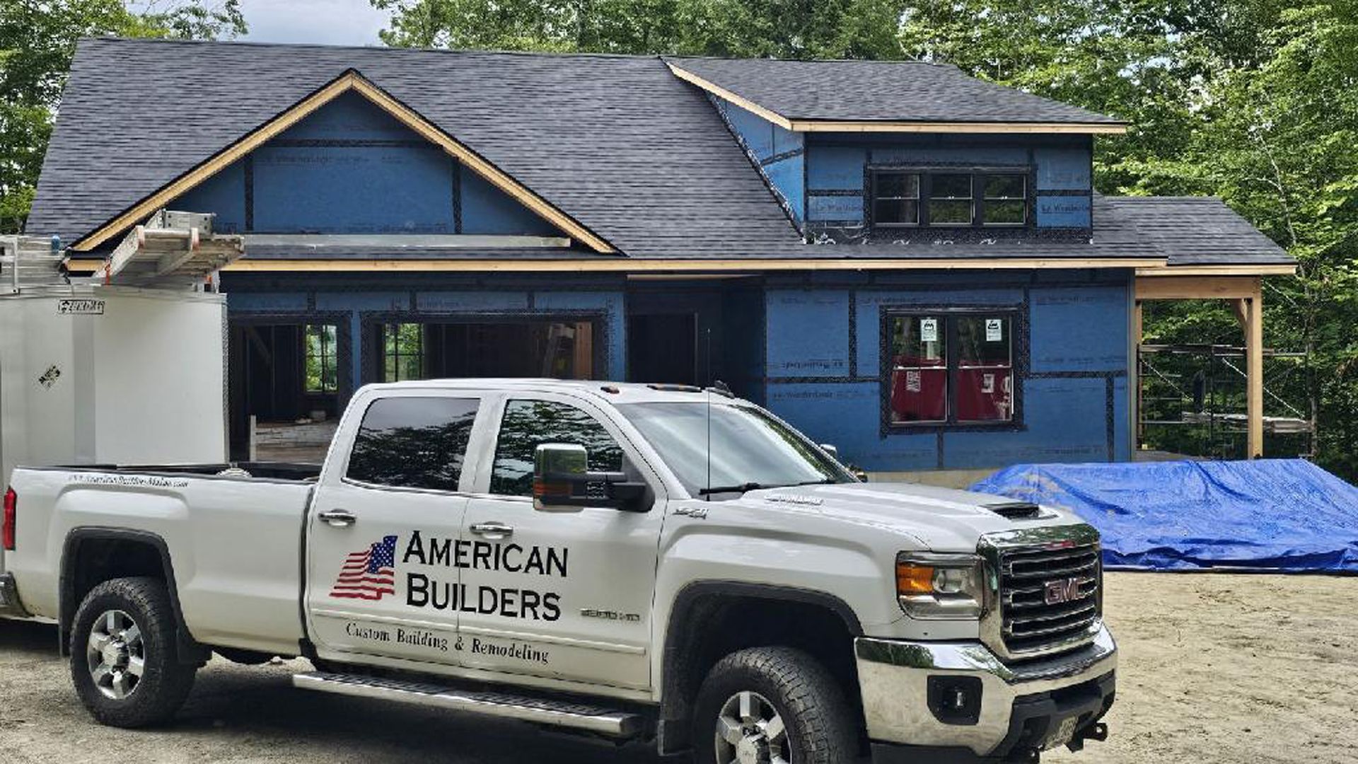 An american builders truck is parked in front of a house under construction.