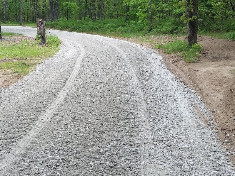 A gravel road going through a forest with trees on both sides.