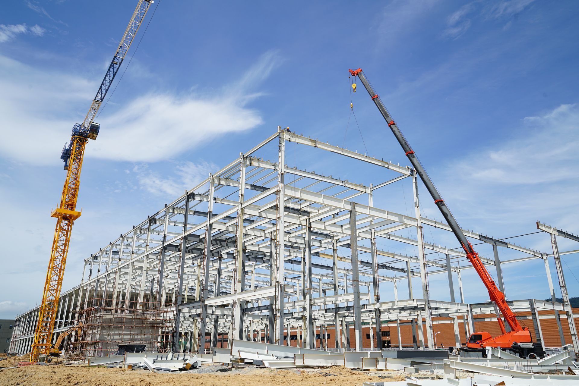 Steel frame construction of a large building, two cranes, blue sky.