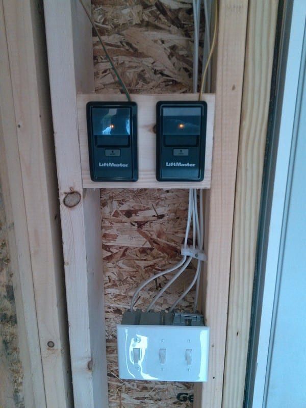 Two garage door remotes are mounted on a wooden wall.