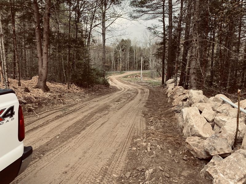 A white truck is parked on the side of a dirt road in the woods.