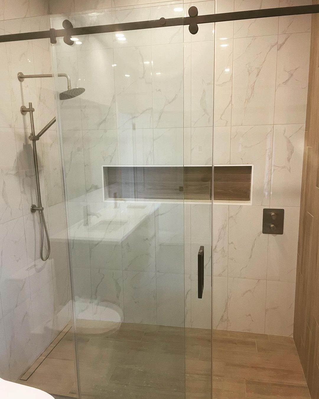 Une salle de bain avec une porte de douche coulissante en verre, un lavabo, des toilettes et un pommeau de douche.