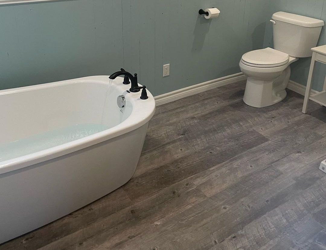 Salle de bain avec baignoire blanche, toilettes et parquet gris imitation bois. Mur bleu.