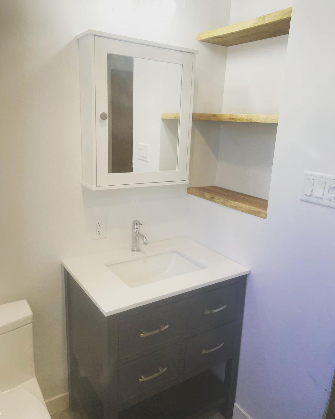 Une salle de bain avec lavabo, WC, miroir et étagères.