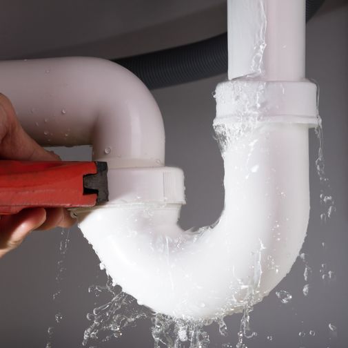 Une personne répare un tuyau qui fuit avec une clé.