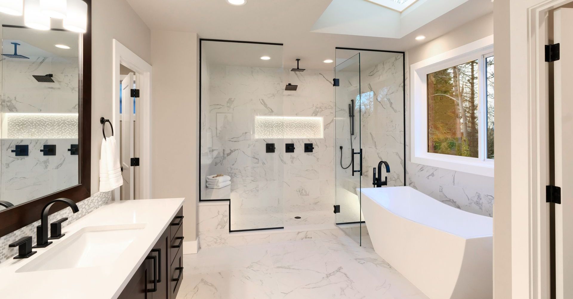 Salle de bains moderne avec murs en marbre, douche en verre, baignoire et robinetterie noire.