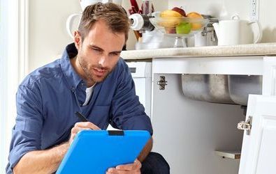 Un homme est agenouillé dans une cuisine et regarde un presse-papiers.