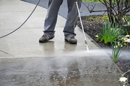 A person is using a high pressure washer to clean a sidewalk.