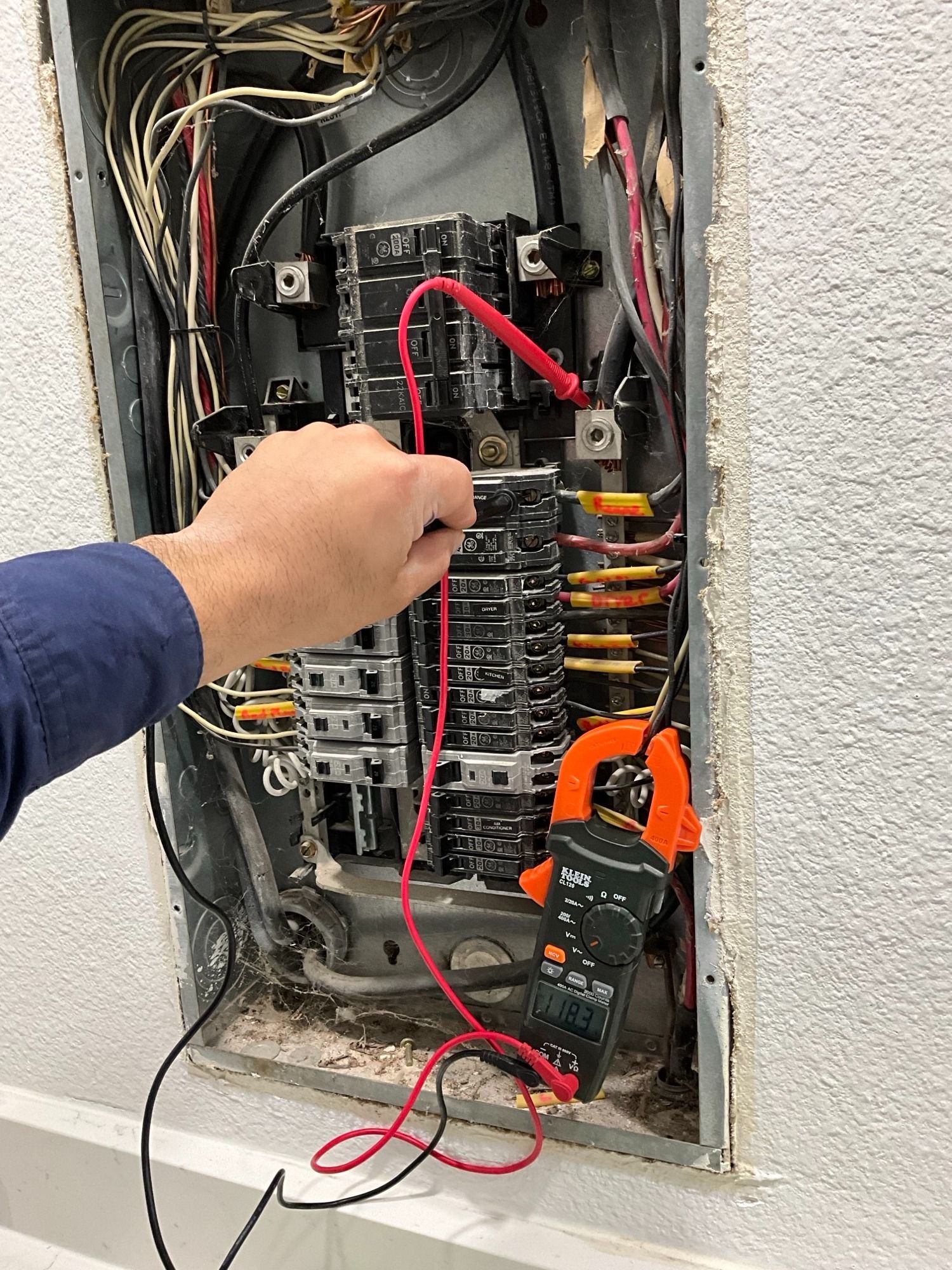 A person is using a clamp meter to test an electrical panel.