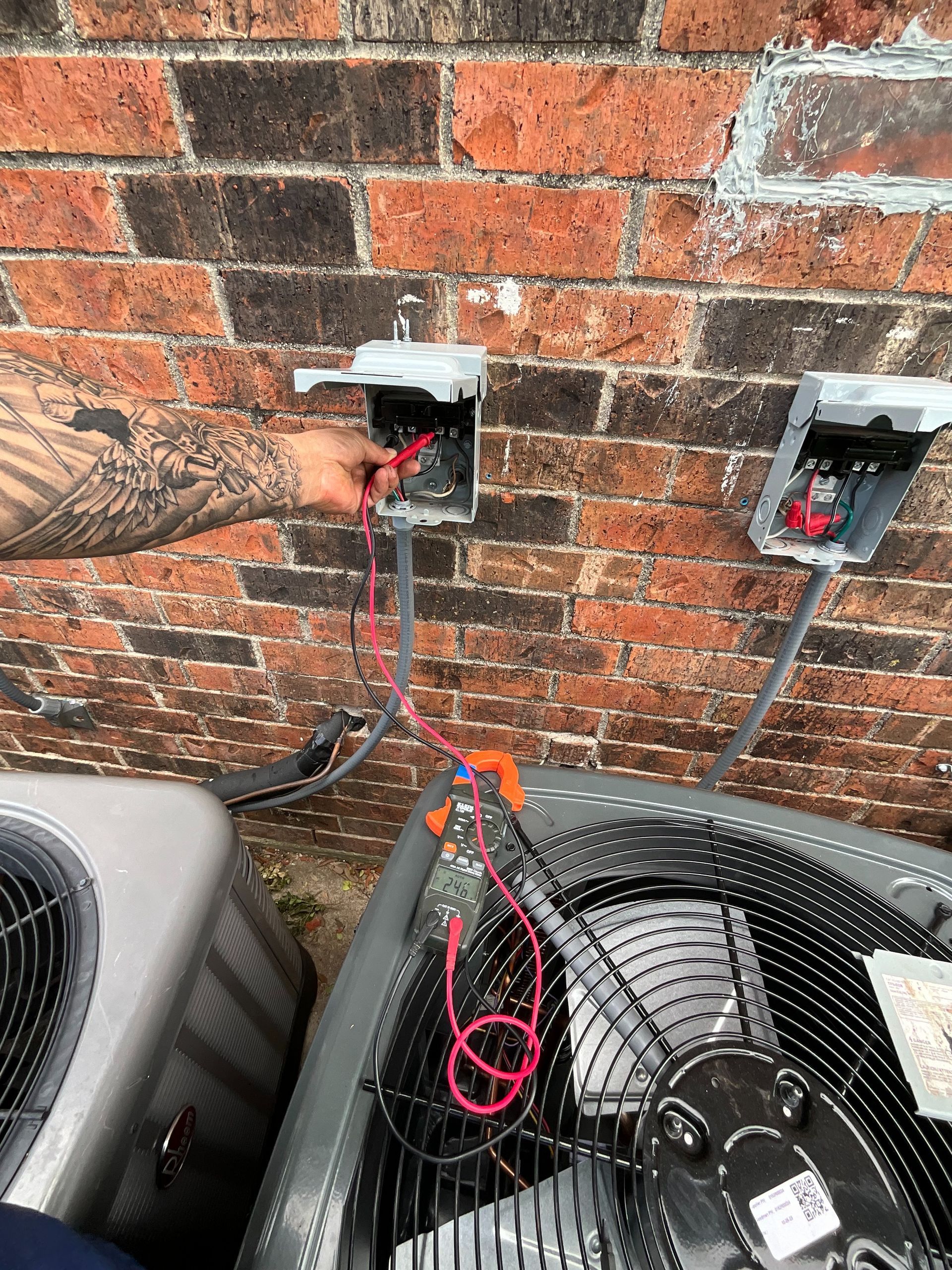 A man is working on an air conditioner outside of a brick building.