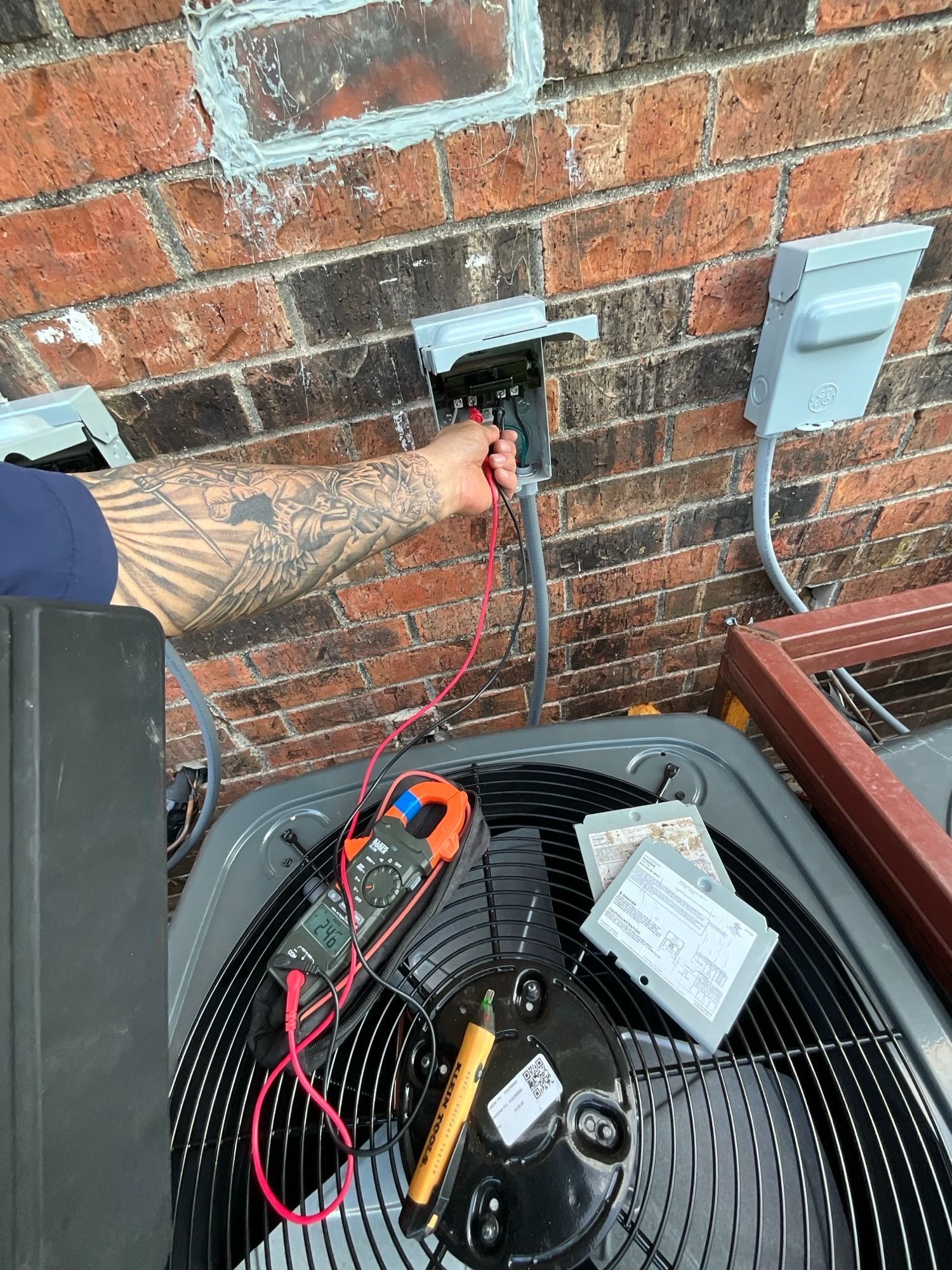 A man is working on an air conditioner outside of a brick building.