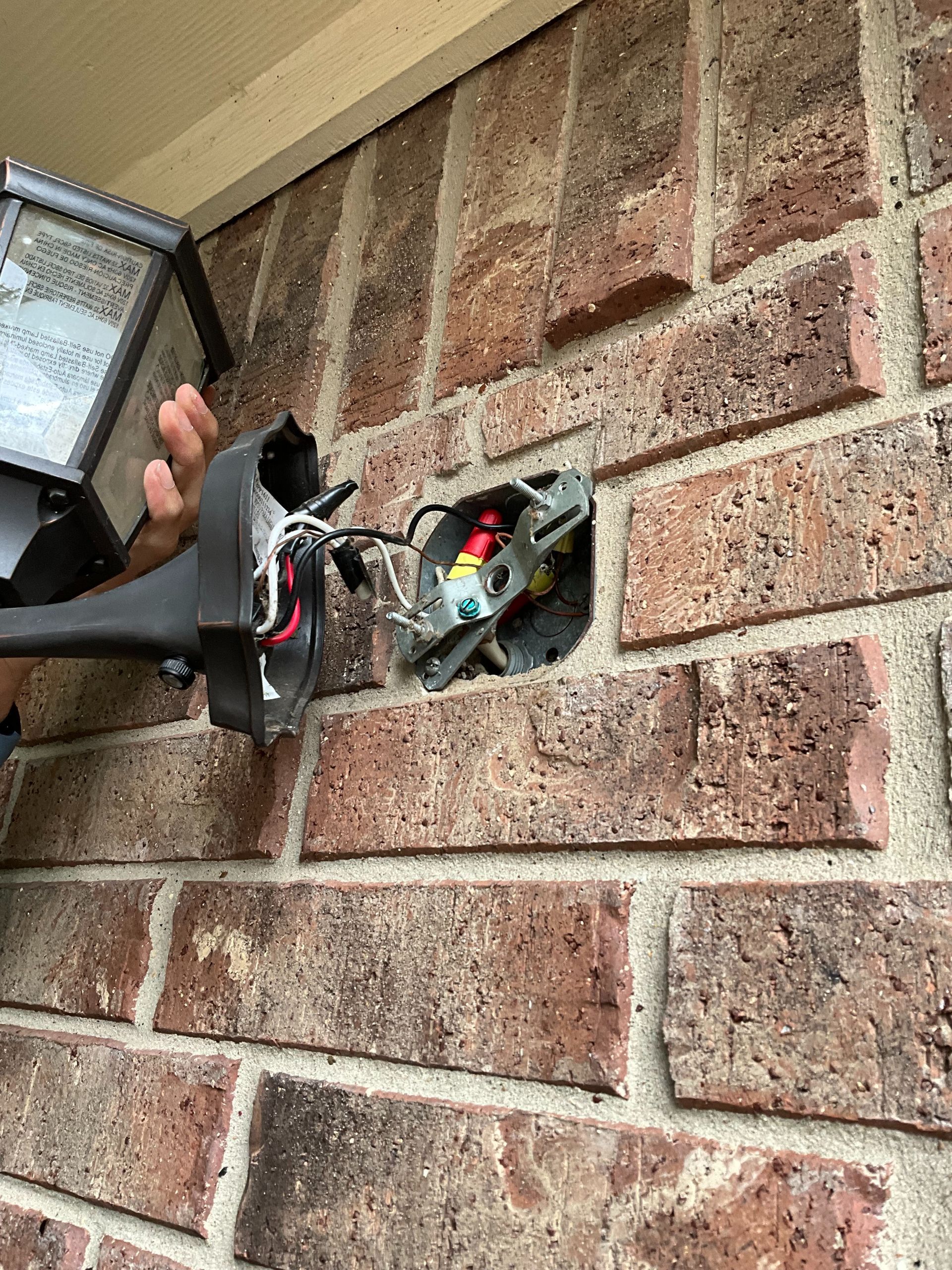 A person is fixing a light on a brick wall.