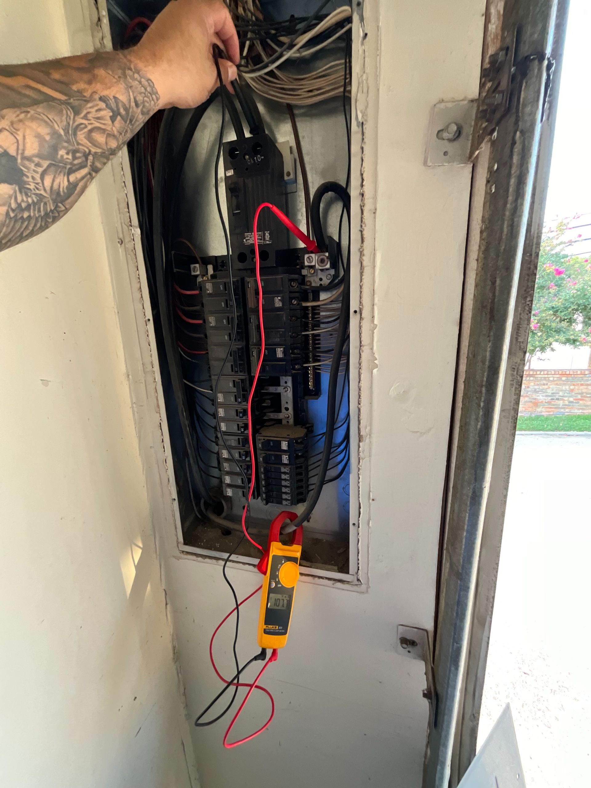 A man is using a clamp meter to test an electrical panel.