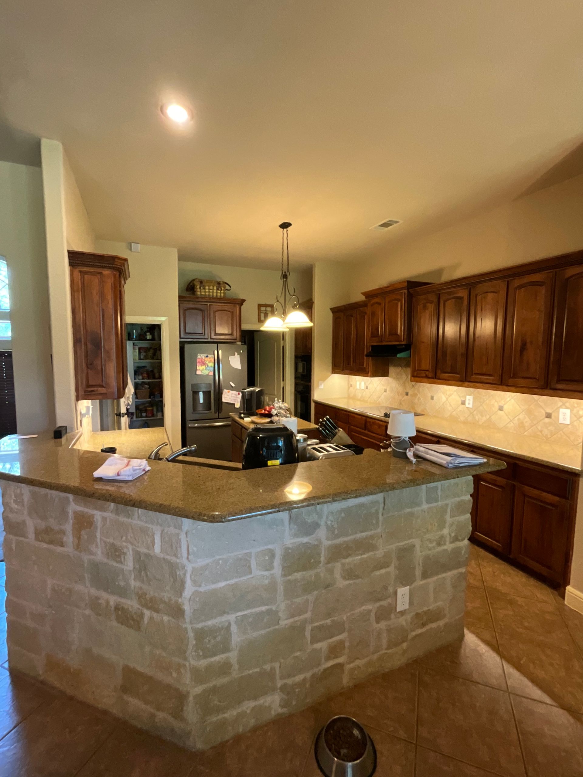 A kitchen with wooden cabinets , granite counter tops , and a brick island.
