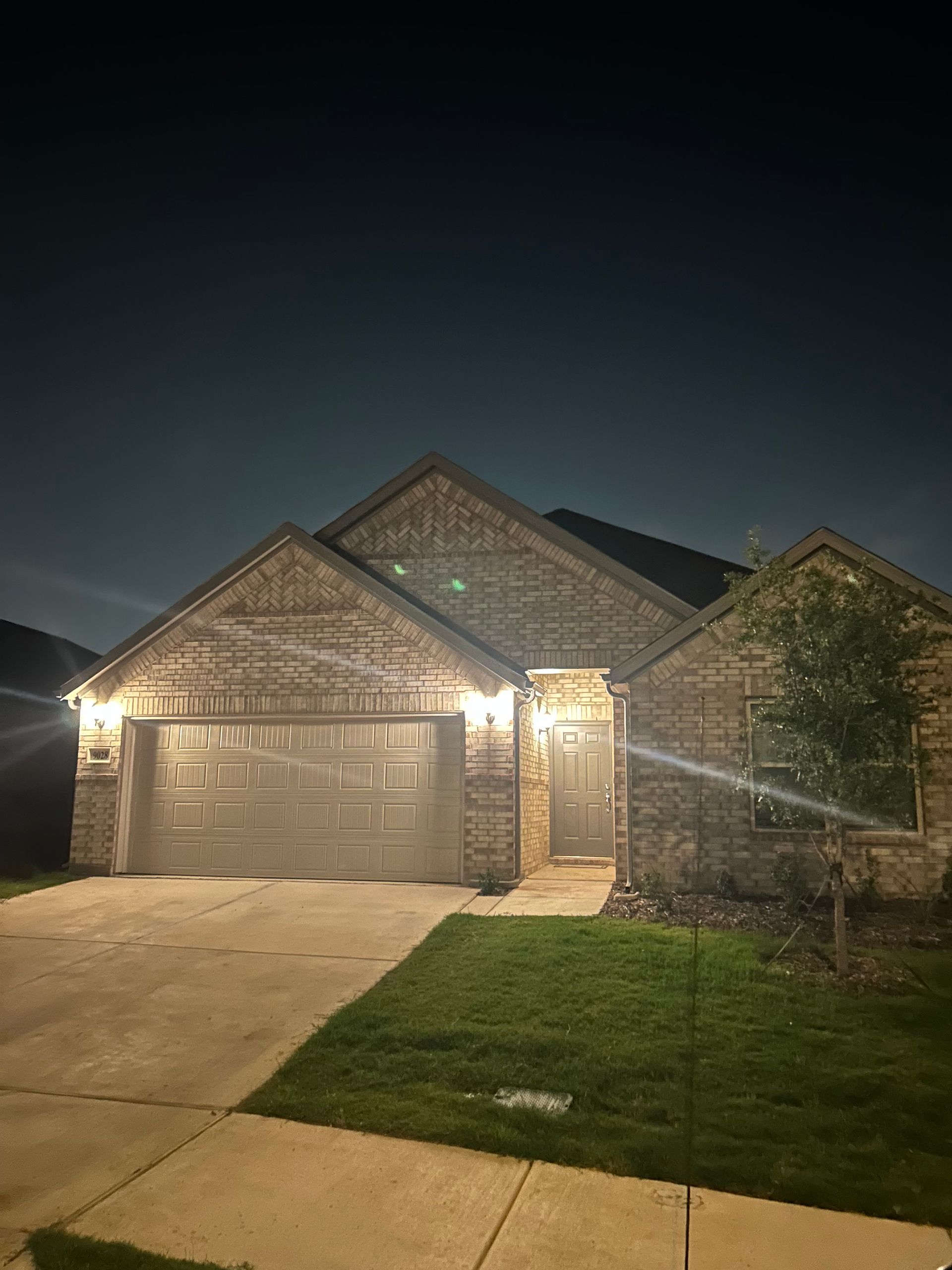 A brick house with two garage doors is lit up at night.