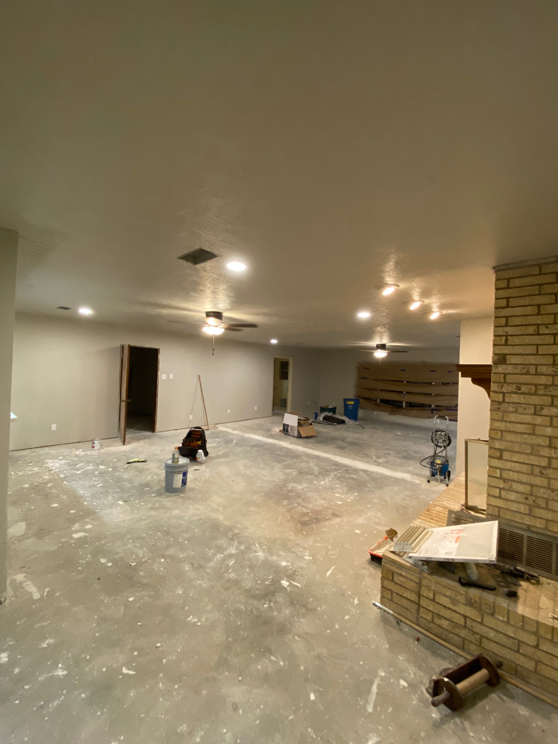 A large empty room with a brick fireplace and a ceiling fan.