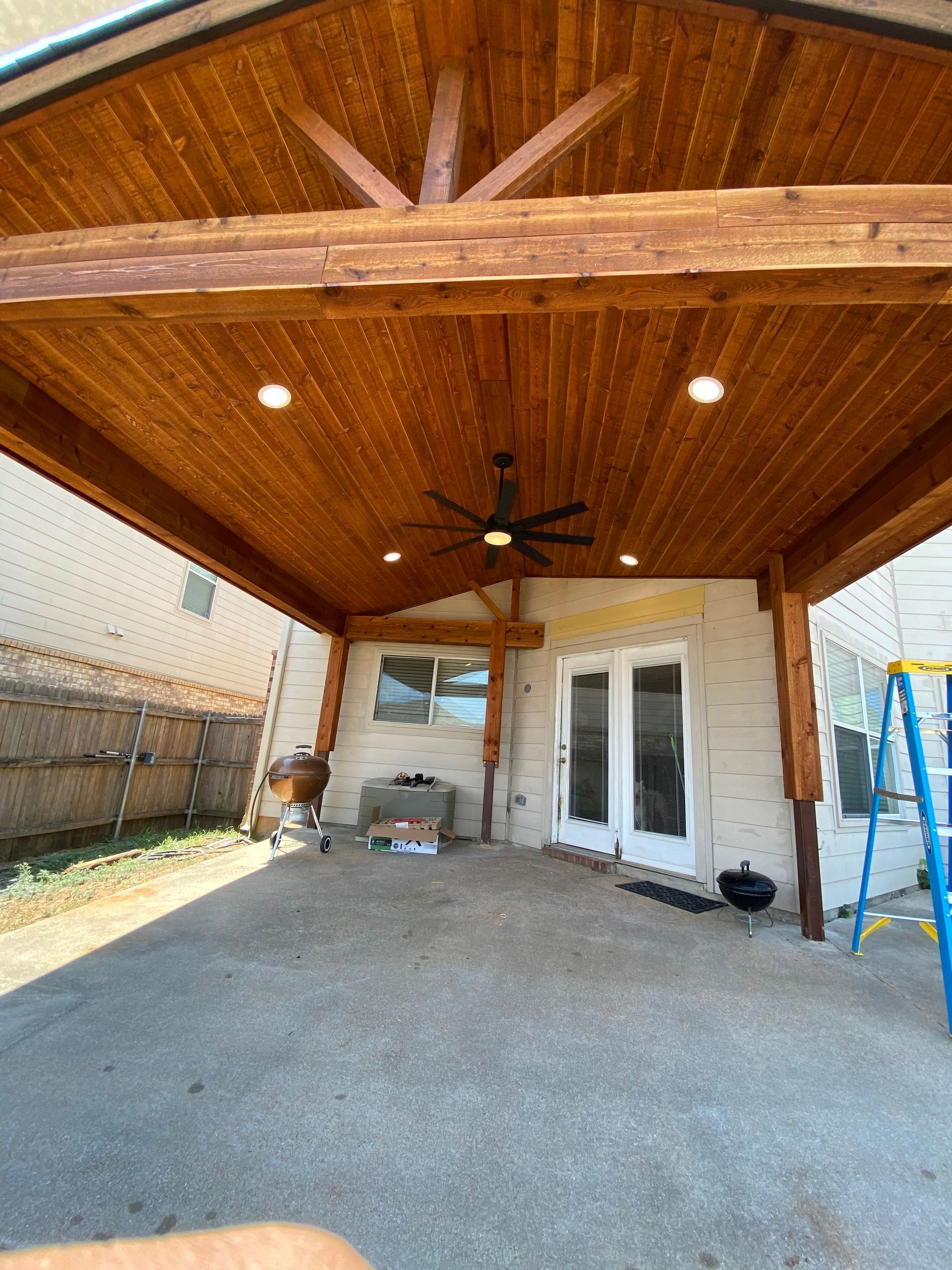 A covered patio with a wooden ceiling and a ceiling fan.