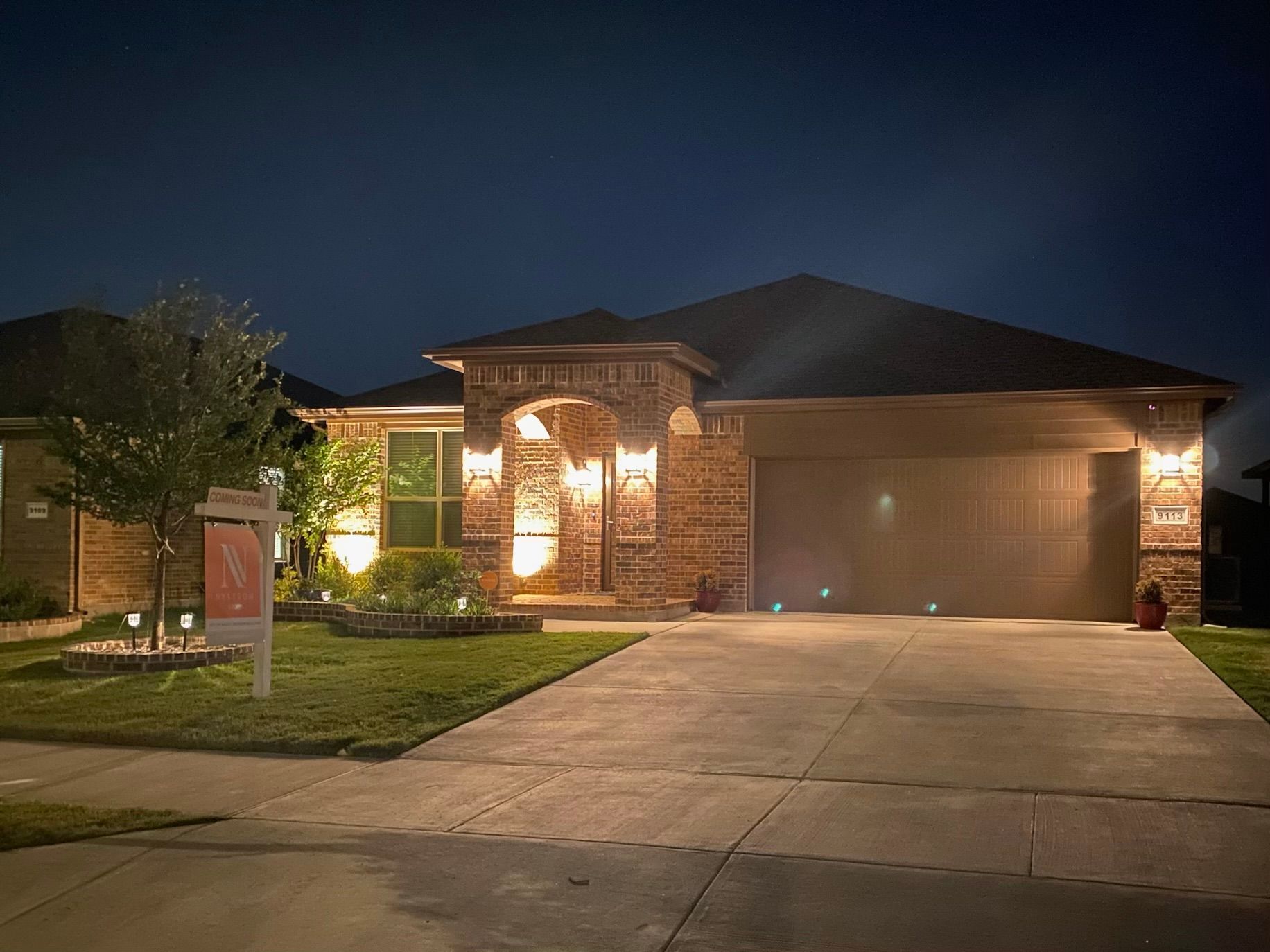 A house is lit up at night with a for sale sign in front of it.