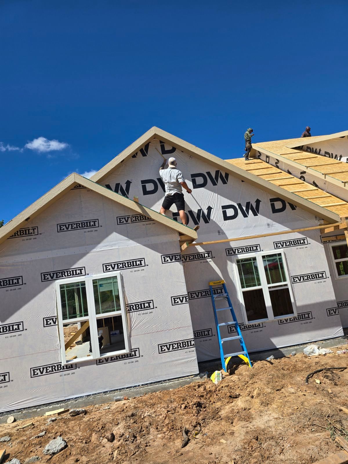 A man is standing on the roof of a house under construction.