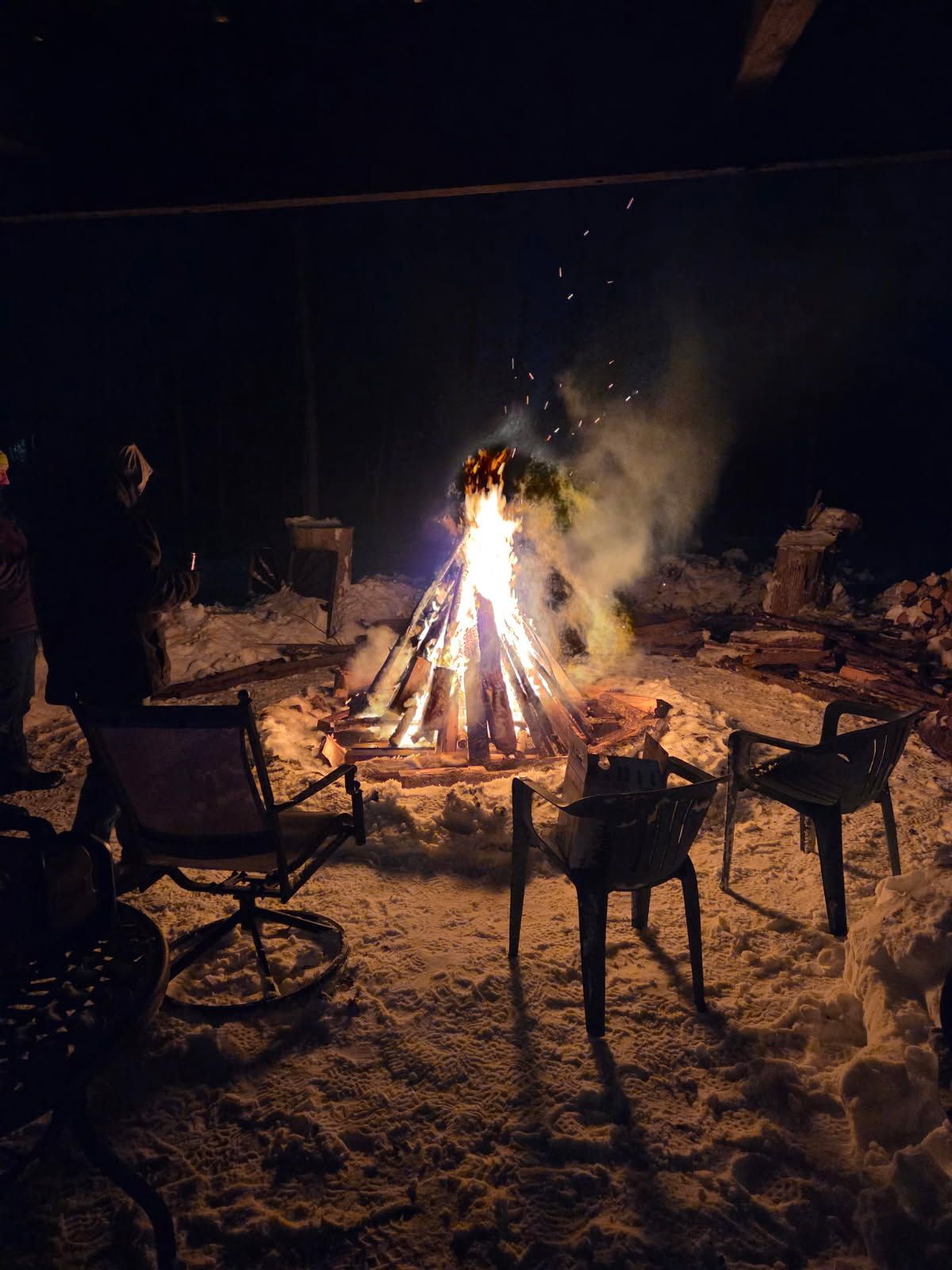 Camping scene: Tent, campfire, and chair on a grassy bank by a river.