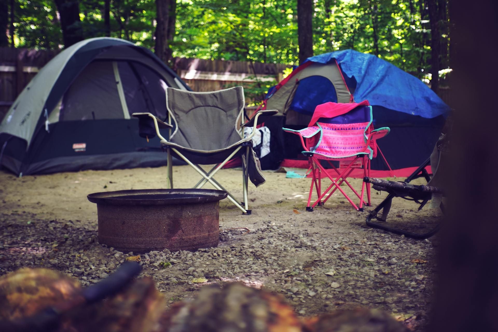 Camping tents line a grassy field by a lake at sunset. Blue, purple, and green tents glow in the warm light.