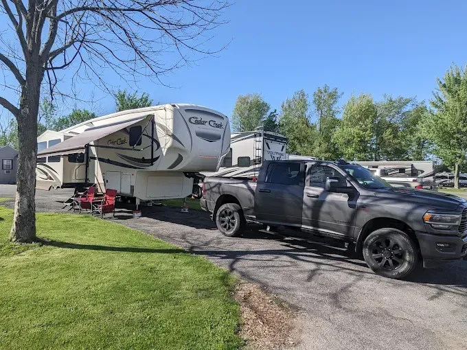 A dark pickup truck towing a large fifth-wheel camper on a grassy campsite.