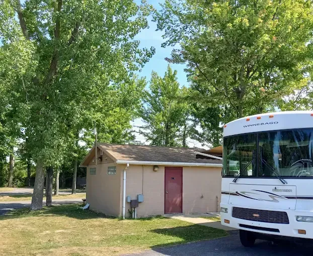 RV parked near a tan restroom building with a red door, trees in the background.