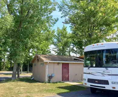 RV parked near a tan restroom building with a red door, trees in the background.