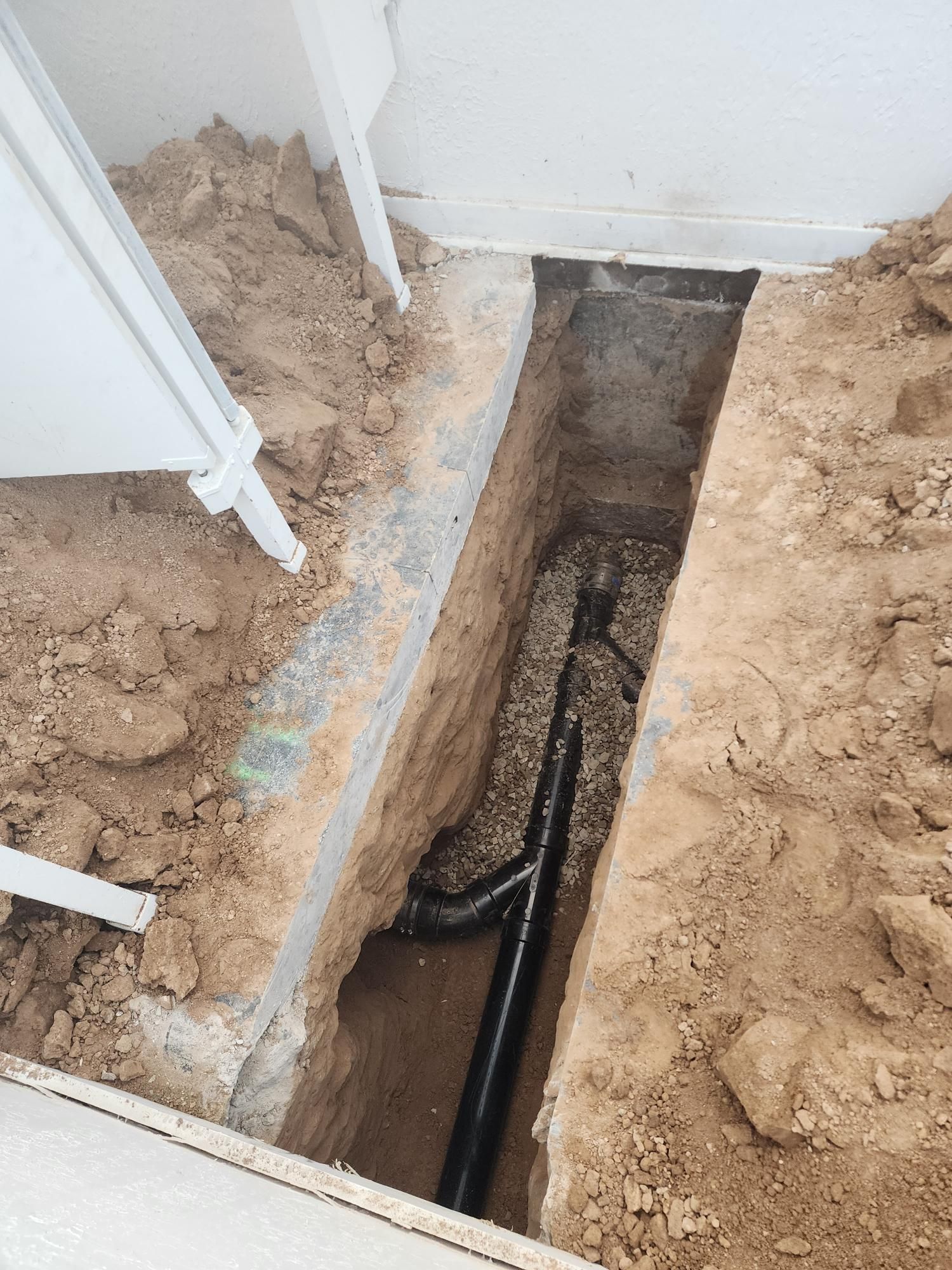 Trench dug into the dirt floor for black PVC pipes, likely for plumbing work inside a building.