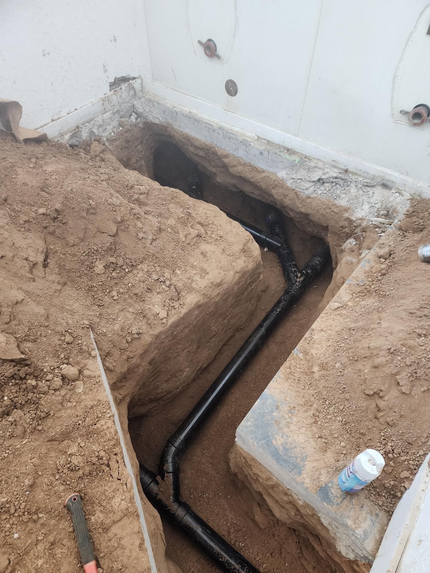 Black pipes in a trench for plumbing against a concrete structure and dirt.