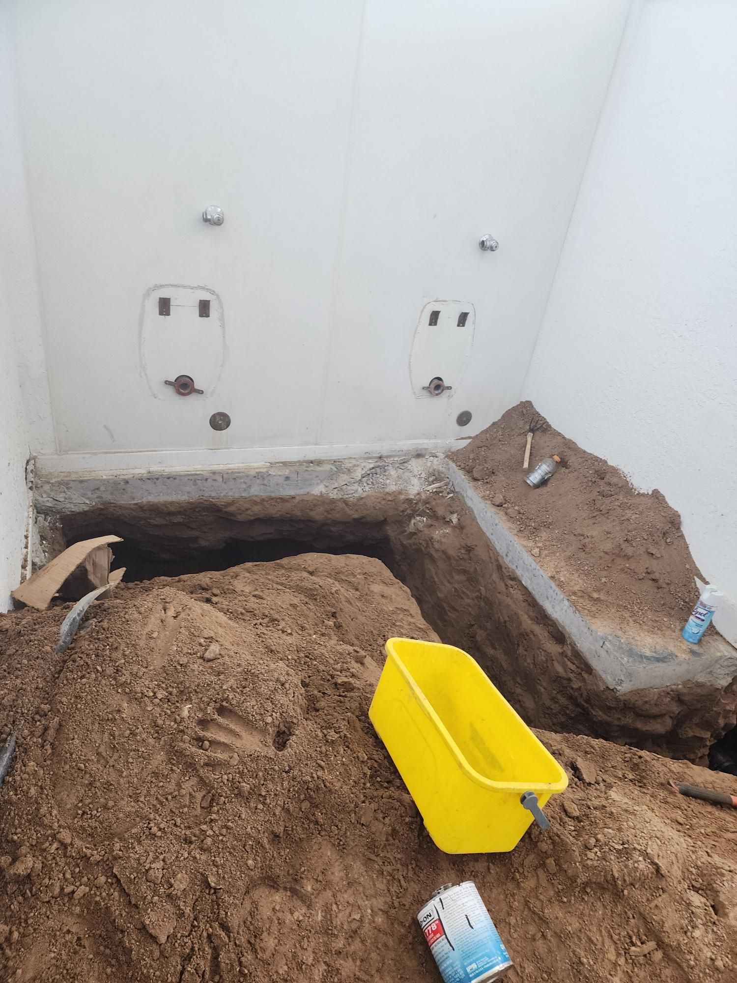 Construction site: Interior room with exposed plumbing fixtures, dirt mound, yellow bucket.
