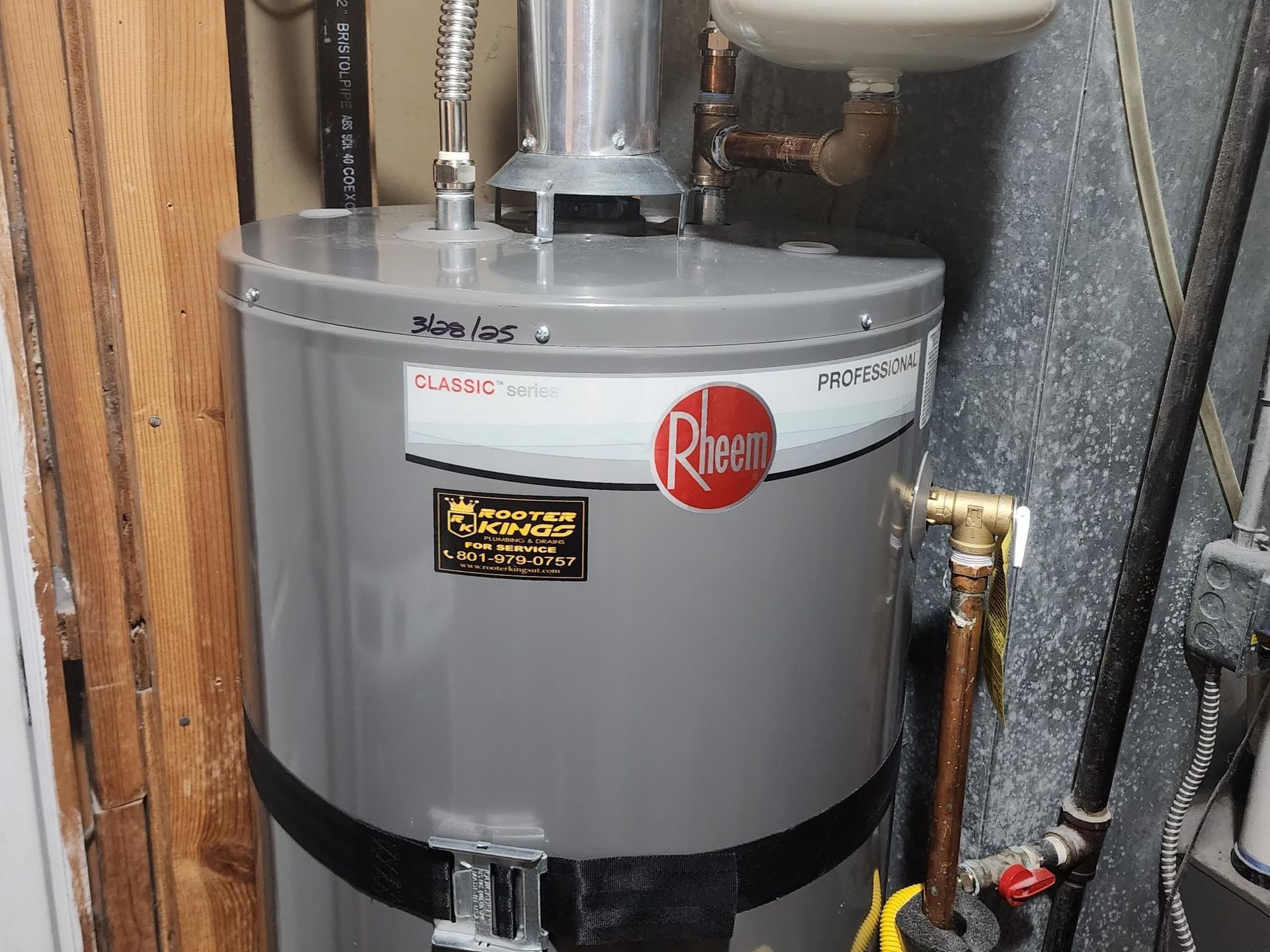 A gray Rheem water heater in a utility room. Pipes and connections visible.