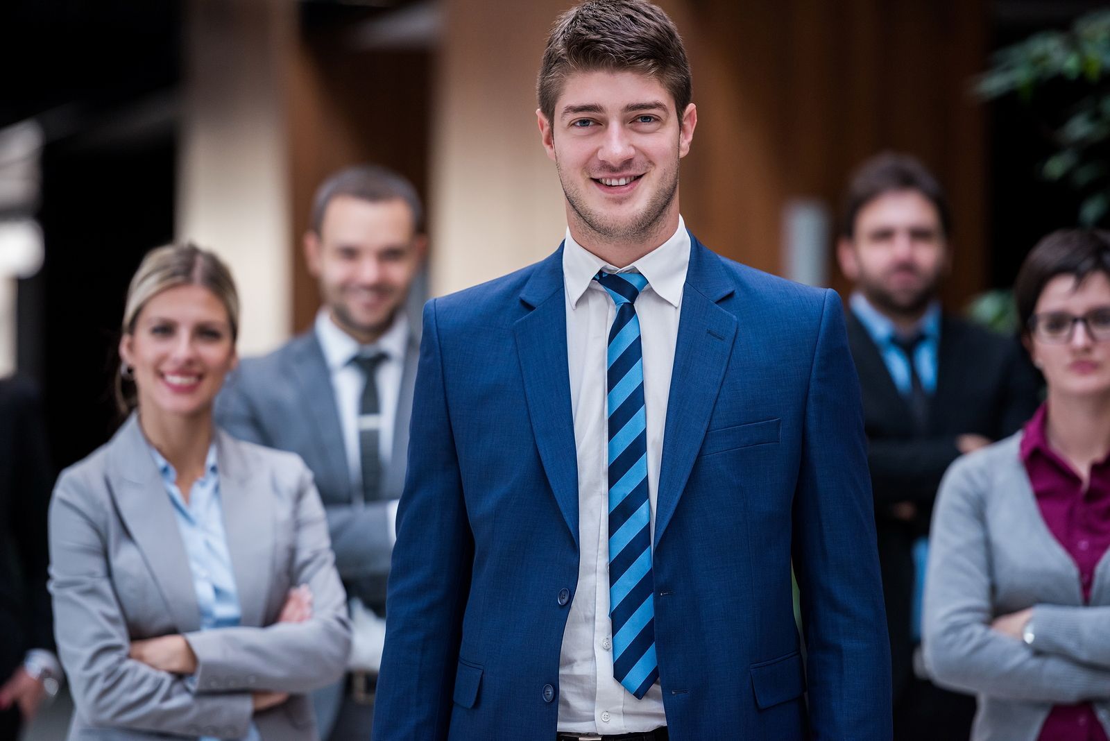 Een groep van negen personen in zakelijke kleding viert feest met opgeheven armen.