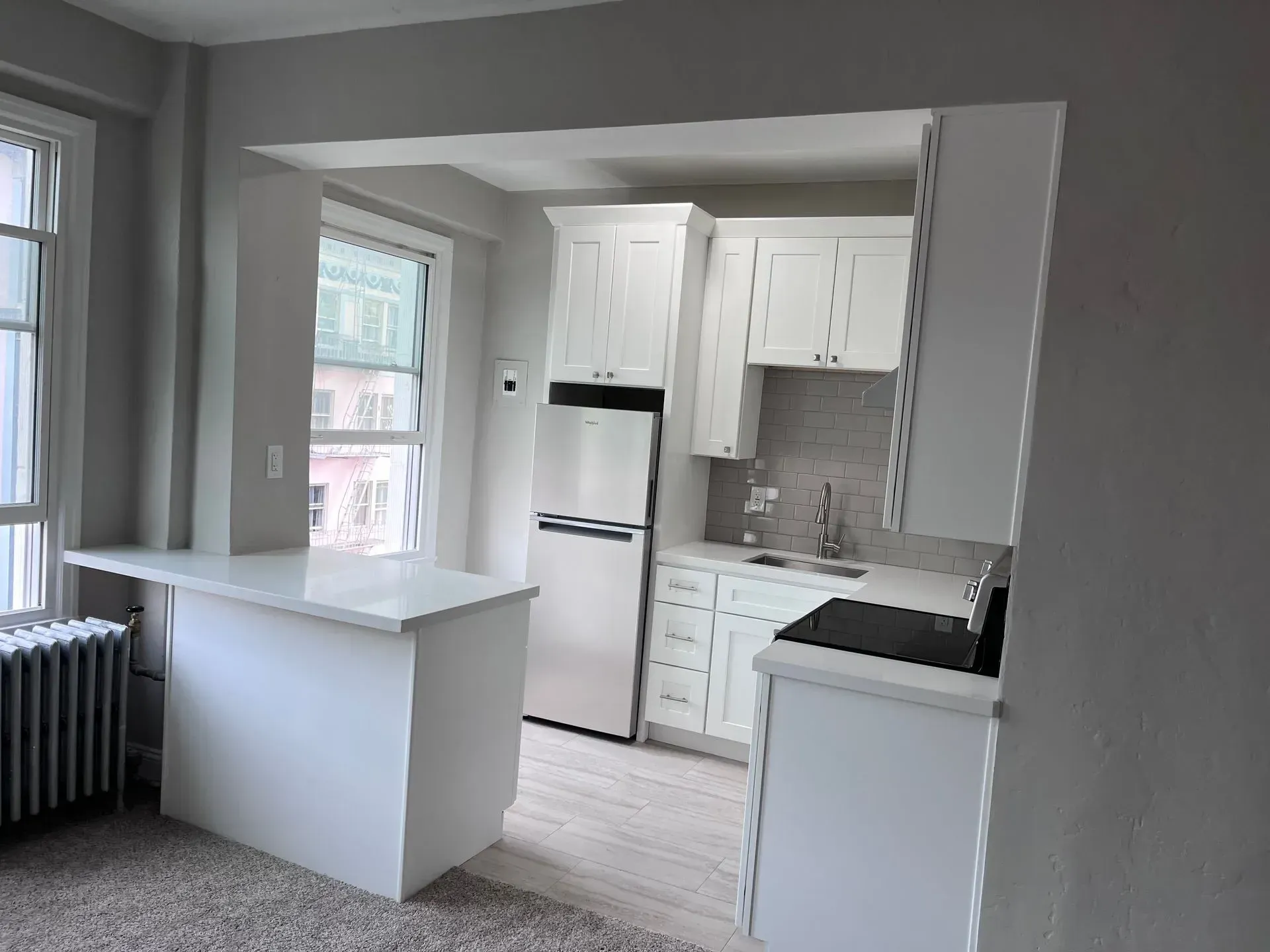 White kitchen with breakfast bar, refrigerator, and cabinetry under a window.