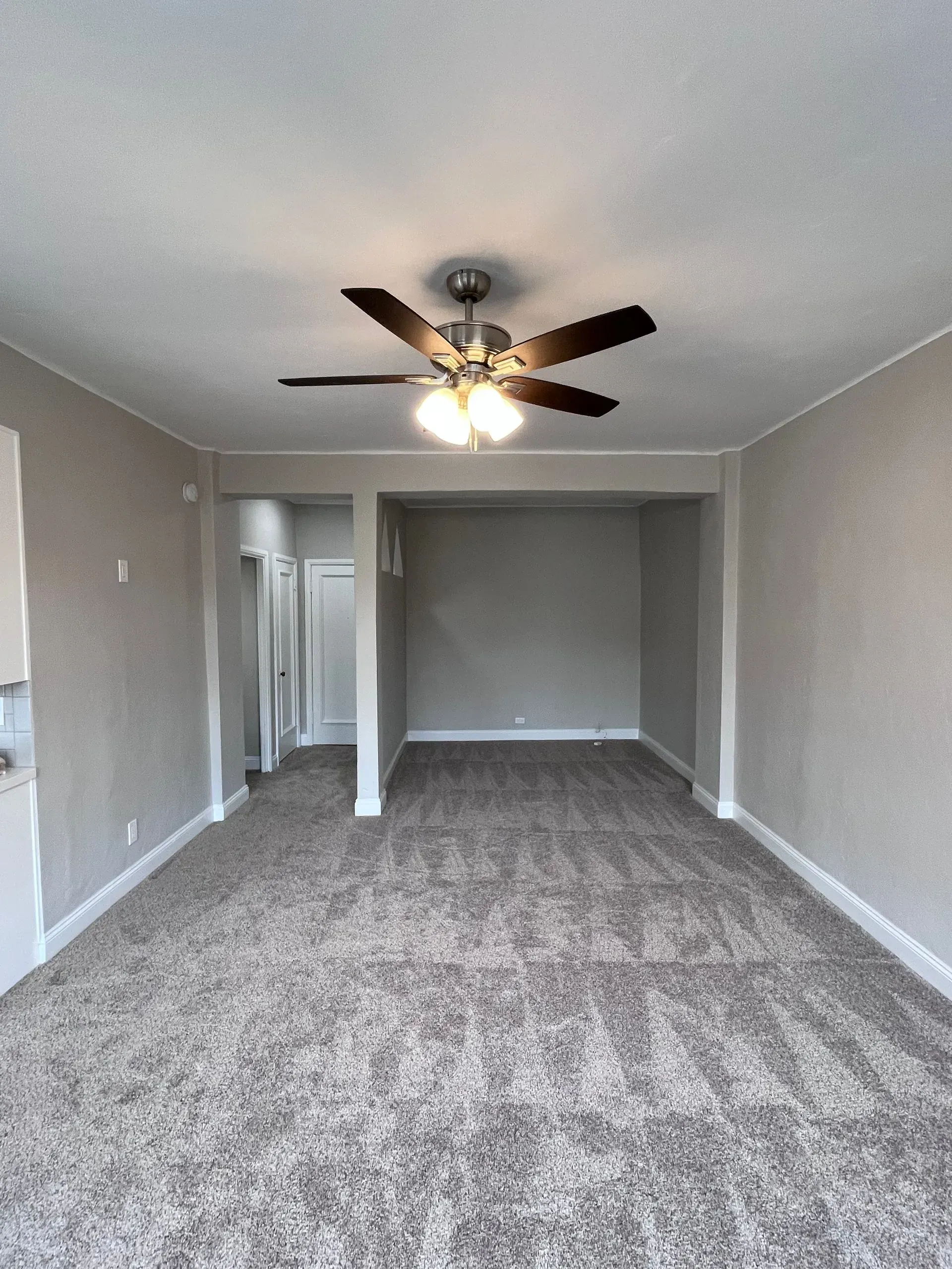 Empty room with gray carpet, walls, and ceiling, with a ceiling fan.