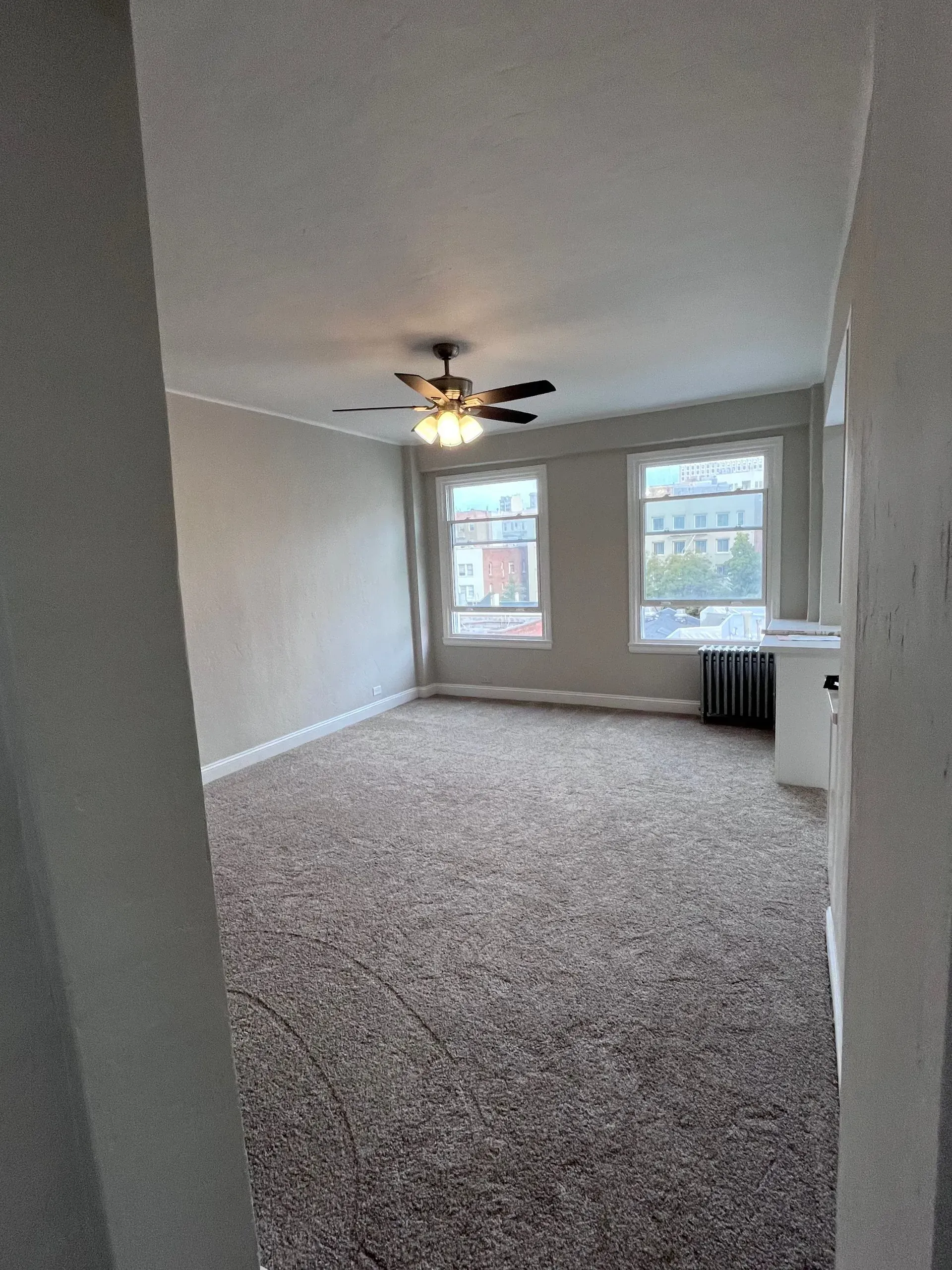 Empty room with carpet, two windows, and a ceiling fan.