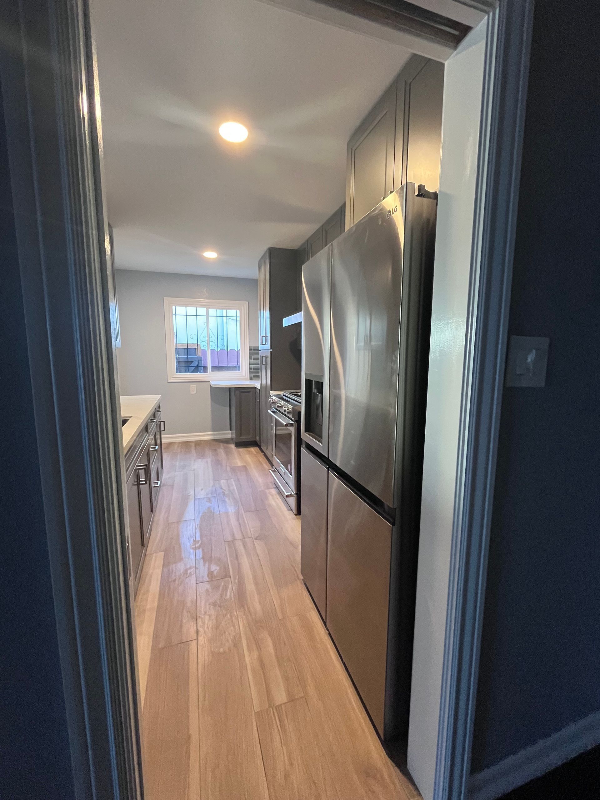 Narrow kitchen with gray cabinets, stainless steel refrigerator, and wood floor.