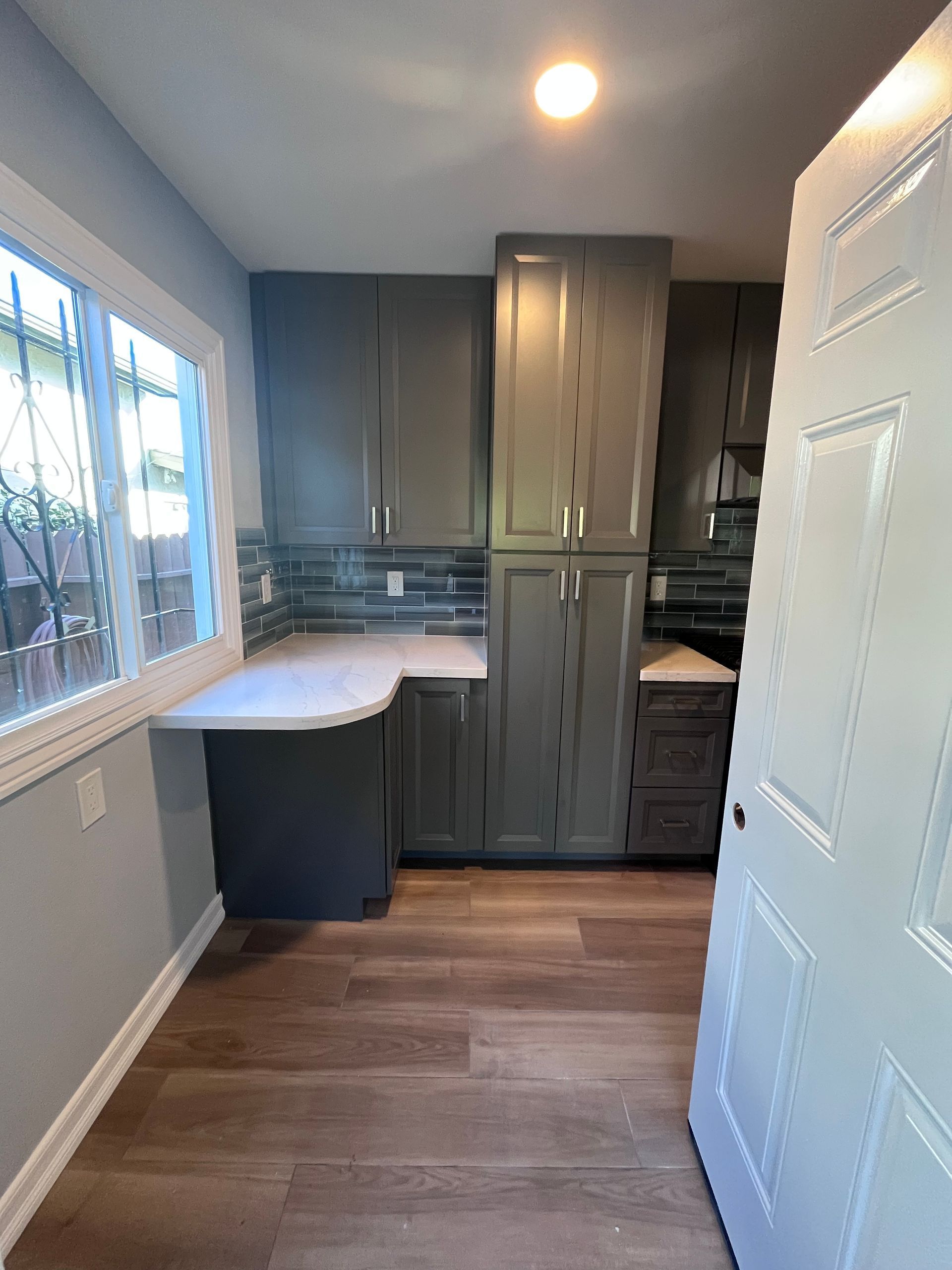 Kitchen with gray cabinets, wood-look floor, countertop, and window.