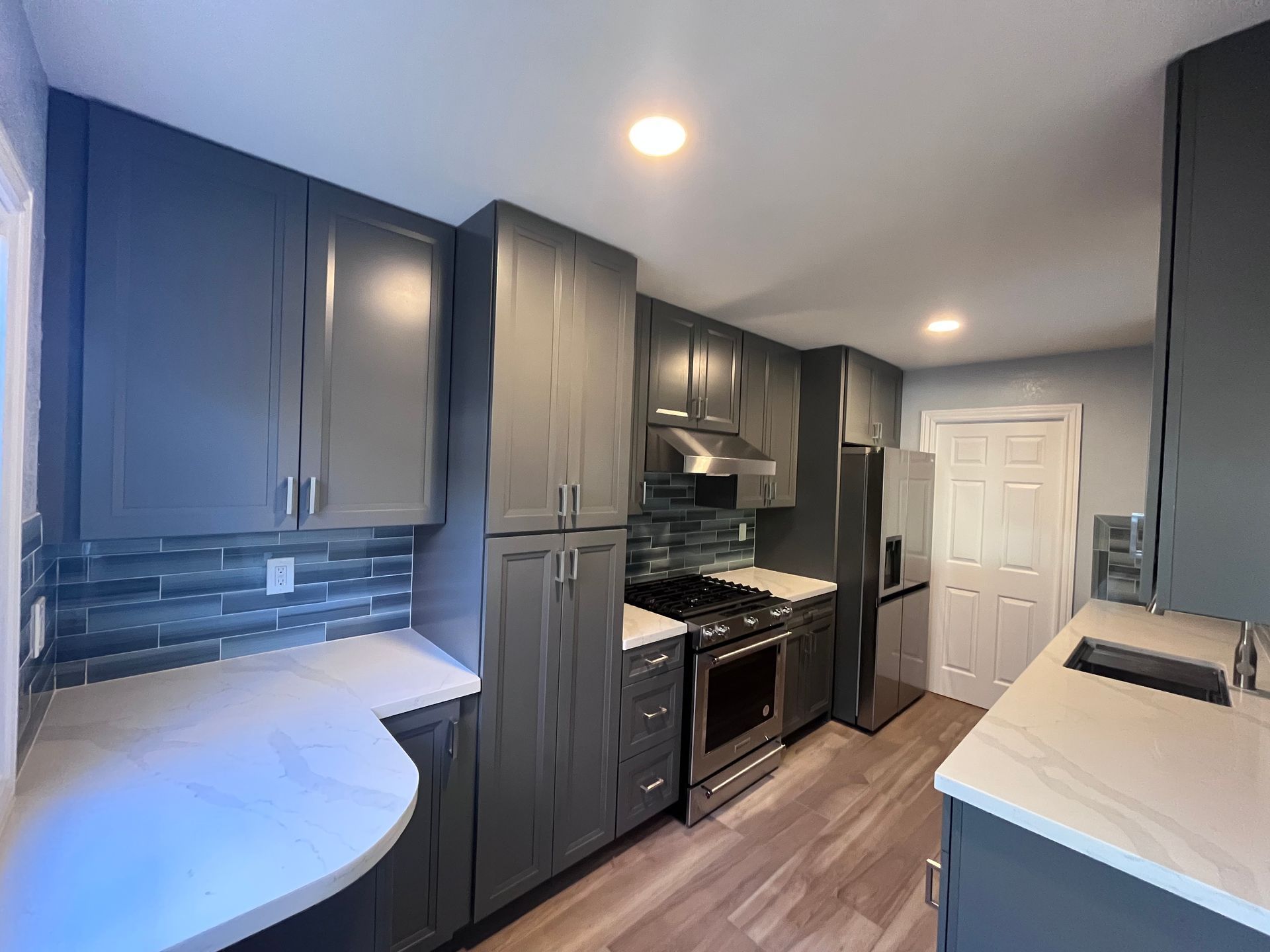 Gray kitchen cabinets, stainless steel appliances, white countertops, and wood-look flooring.