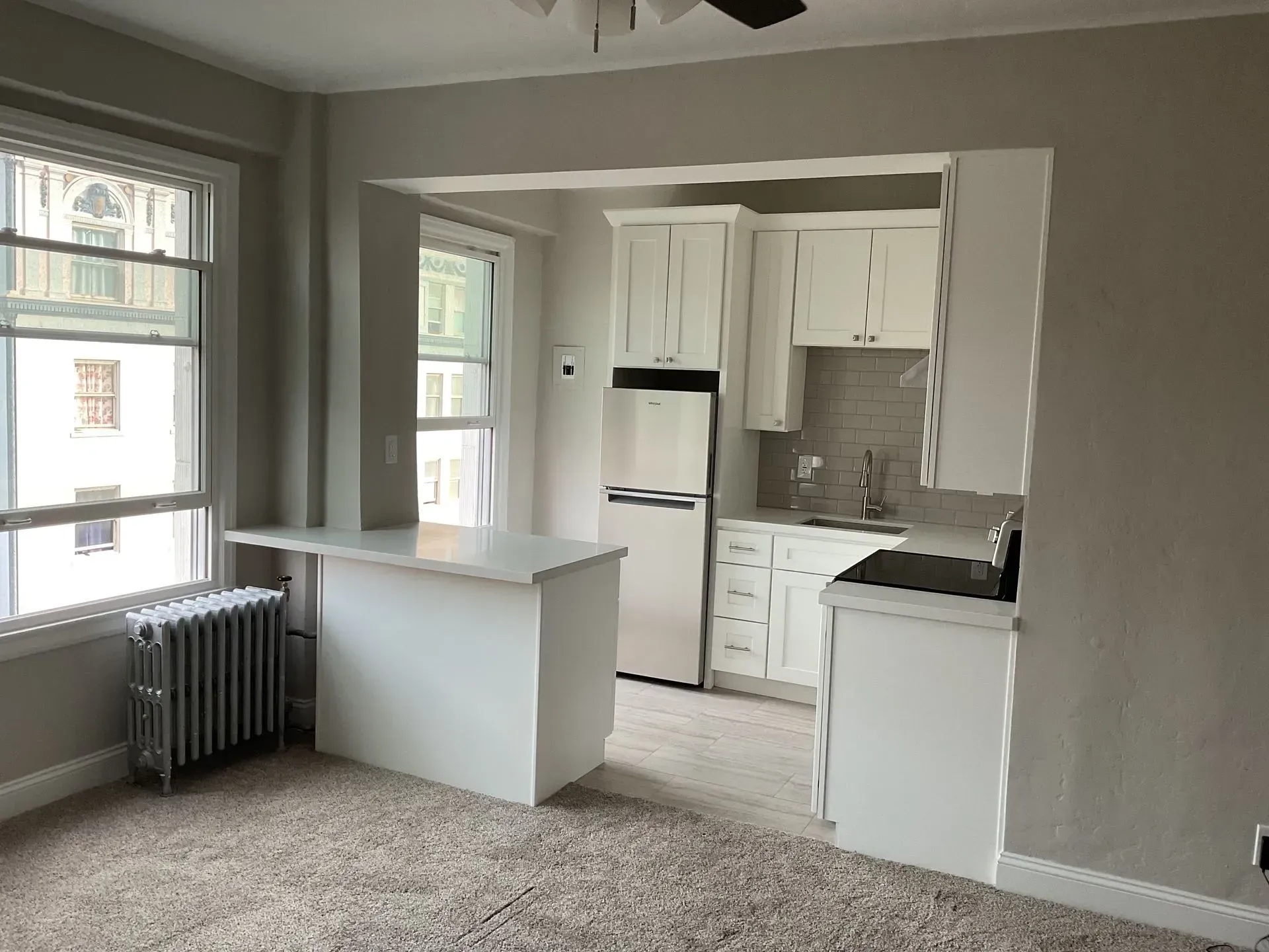 Small kitchen in an apartment, with white cabinets, breakfast bar, and window.