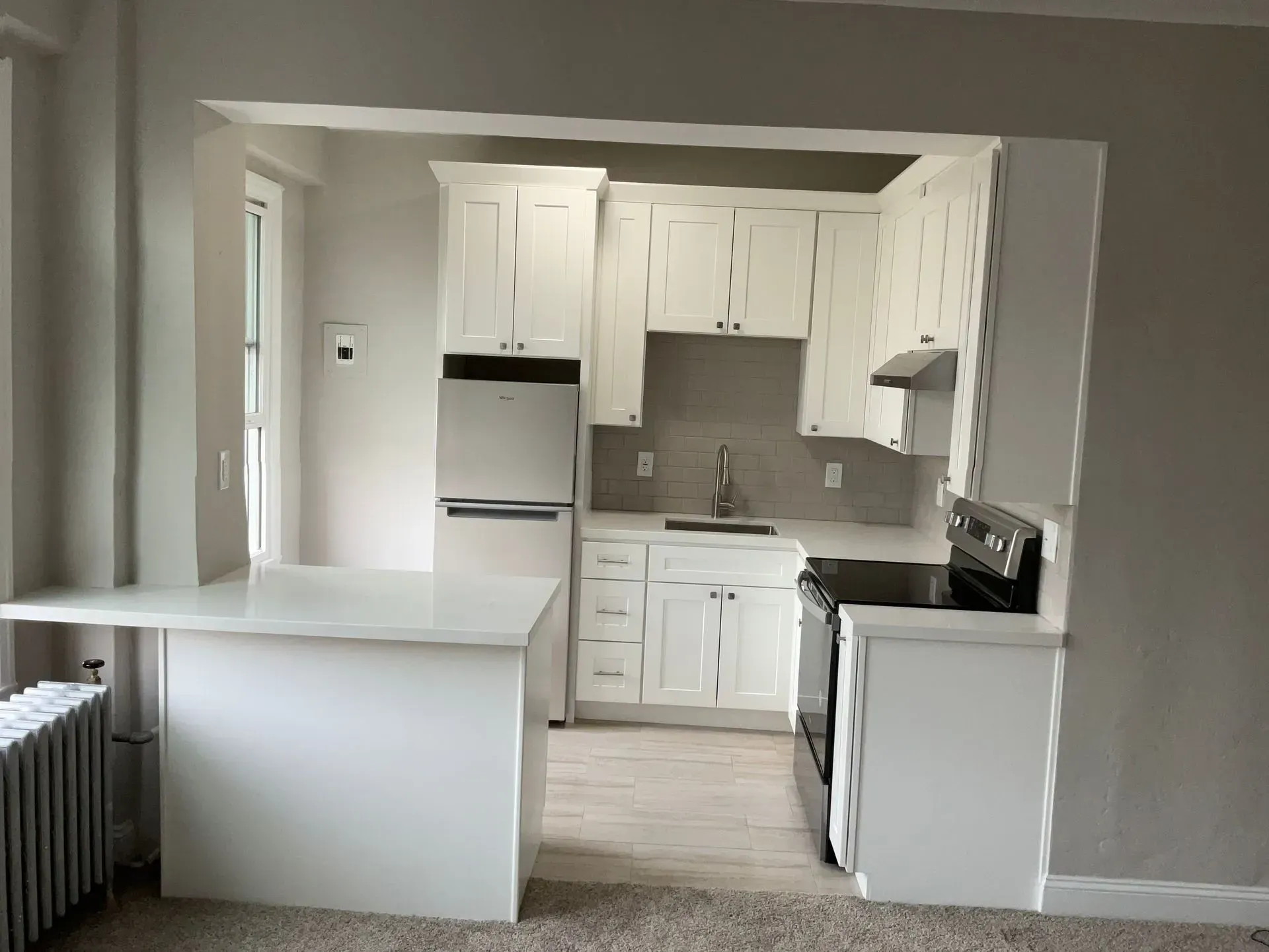 White kitchen with countertops, cabinets, refrigerator, and stove. A breakfast bar is on the left.