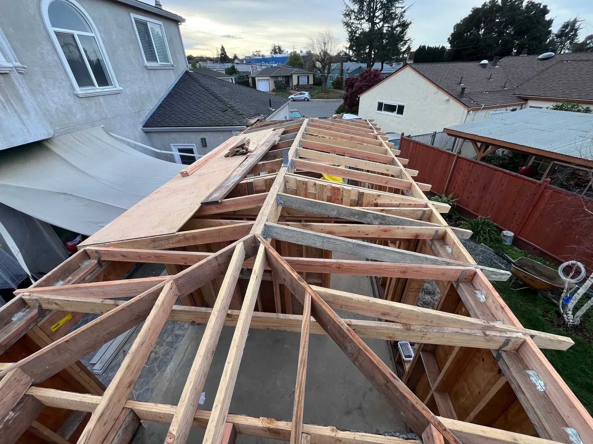 Wooden roof frame under construction with surrounding houses and trees.