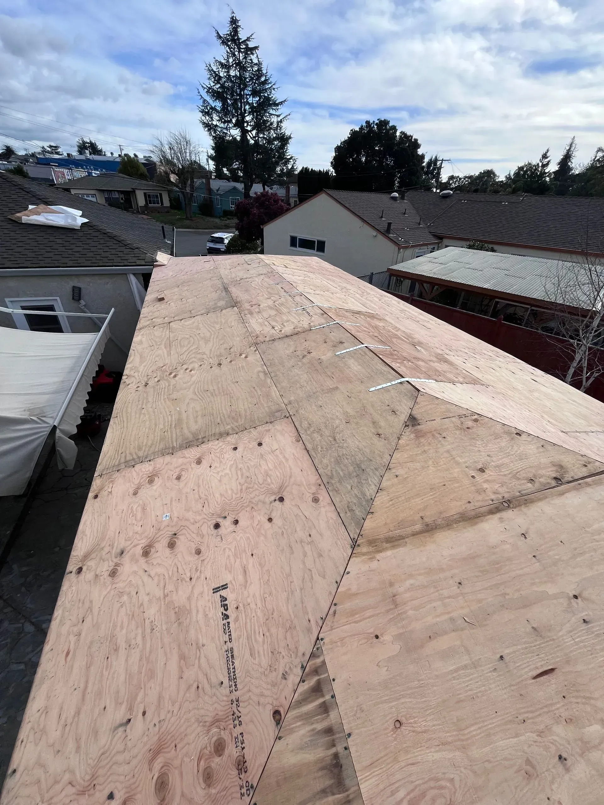 View of a wooden roof under construction with several surrounding houses and a cloudy sky.