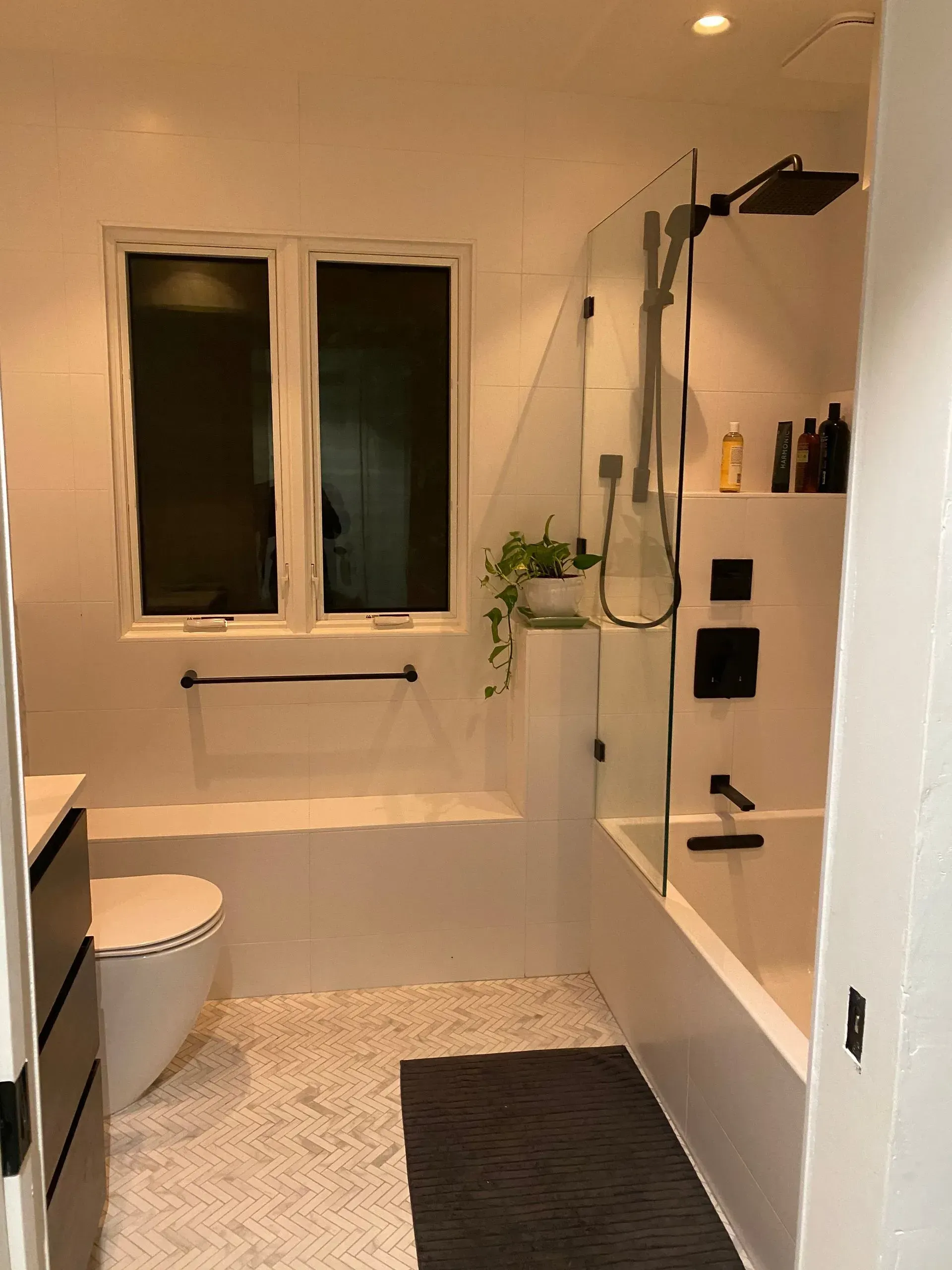Modern white bathroom with tub, shower, and window. Black fixtures, tiled walls, and patterned floor.
