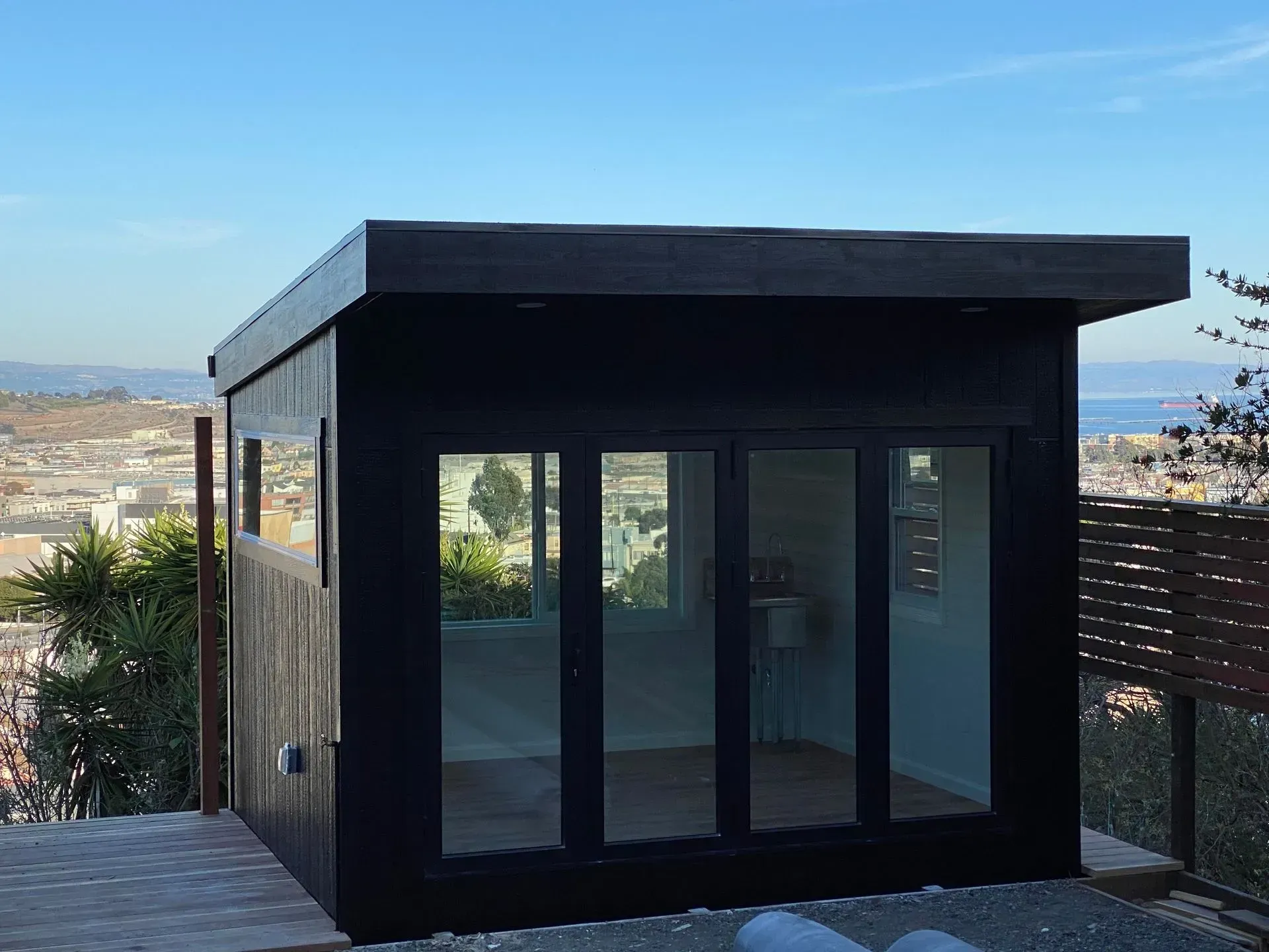 Black modern shed with glass doors and windows, overlooking a city.