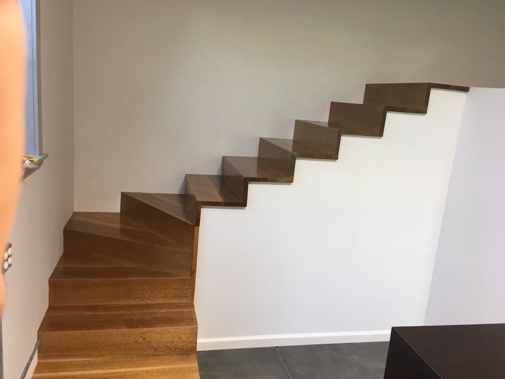 Wooden floating stairs against a white wall; brown treads, gray floor.