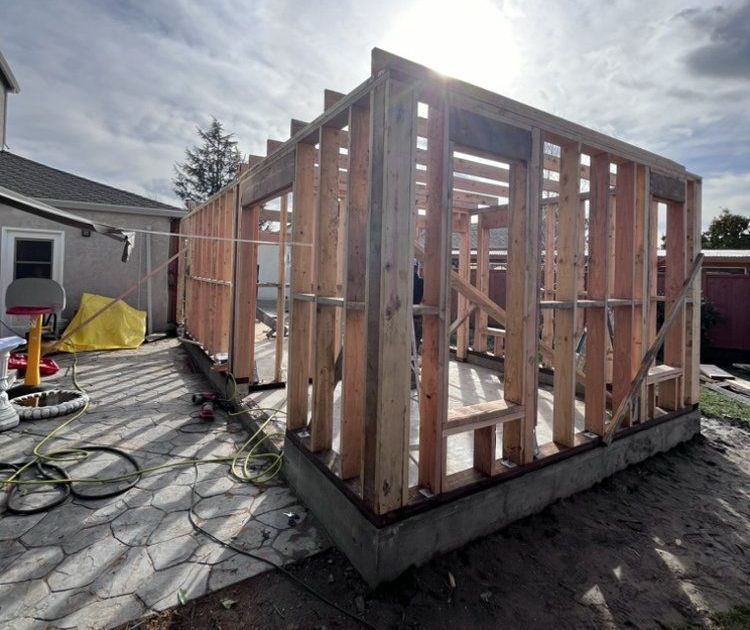 Wooden frame of a building under construction on a concrete foundation, outdoors on a cloudy day.